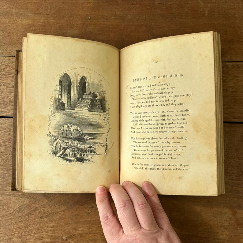 May include: An open antique book with aged, yellowed pages. The left page features two black and white illustrations, one of a building with arches and the other of a landscape. The right page contains printed text, with the title "POWE OF THE CHURCHYARD."