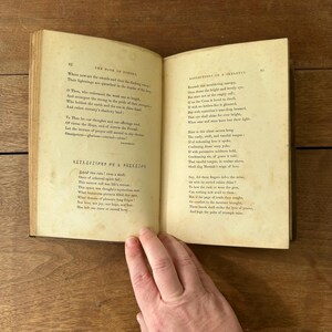 May include: An open antique book with aged, yellowed pages. The left page features the title "REFLECTIONS ON A SKELETON" and poetry. The right page continues the poem. The book is held open by a hand.