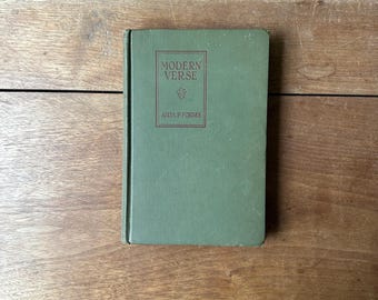 May include: A vintage hardcover book titled "Modern Verse" by Anita P. Forbes. The book has a green cover with the title and author's name in a darker shade of green. The book is resting on a wooden surface.