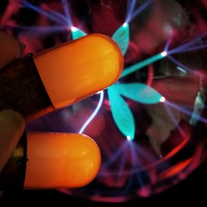 May include: Two orange capsules with a clear glass sphere in the background. The sphere has blue and pink electrical discharges emanating from the center.