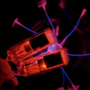 May include: Two red glass tubes with glowing filaments are positioned in front of a blue and pink plasma ball.