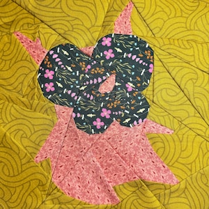 May include: A quilt block with a pink and red floral pattern in the center, surrounded by a yellow and gold patterned fabric.