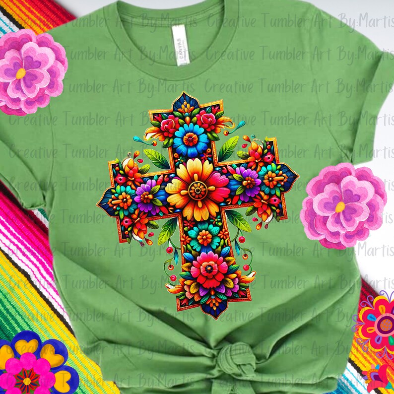 May include: A green t-shirt with a colorful floral cross design. The cross is made up of flowers in shades of red, orange, yellow, pink, blue, and green. The flowers are arranged in a symmetrical pattern around the cross.