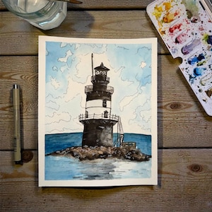 May include: Watercolor painting of a lighthouse on a rocky island. The lighthouse is black and white with a detailed lantern room. The sky is light blue with white cloud outlines, and the sea is a deep blue. A black pen and watercolor palette are in the background.