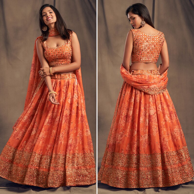 May include: An orange floral print lehenga choli set. The sleeveless top and skirt are adorned with intricate embroidery and embellishments. A matching dupatta is draped over the shoulders. The set is a vibrant and elegant ensemble.