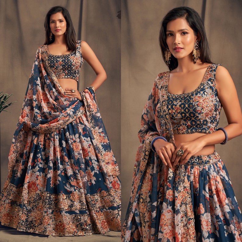 May include: A navy blue floral print lehenga choli set. The sleeveless top and skirt feature a large floral pattern in shades of orange and white. The set includes a matching dupatta. The top has intricate embroidery.