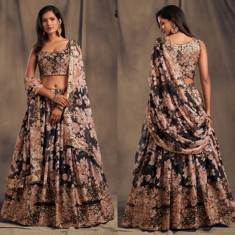 May include: A two-piece floral print outfit featuring a black skirt and a matching top. The skirt and top are adorned with a delicate floral pattern in shades of peach and gold. The outfit includes a matching scarf, and is embellished with gold trim.