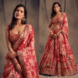 May include: A red floral print lehenga choli ensemble. The outfit features a sleeveless top and a flowing skirt, both adorned with a delicate white floral pattern. The dupatta, or scarf, mirrors the design, with gold embellishments adding a touch of elegance. The outfit is suitable for special occasions.