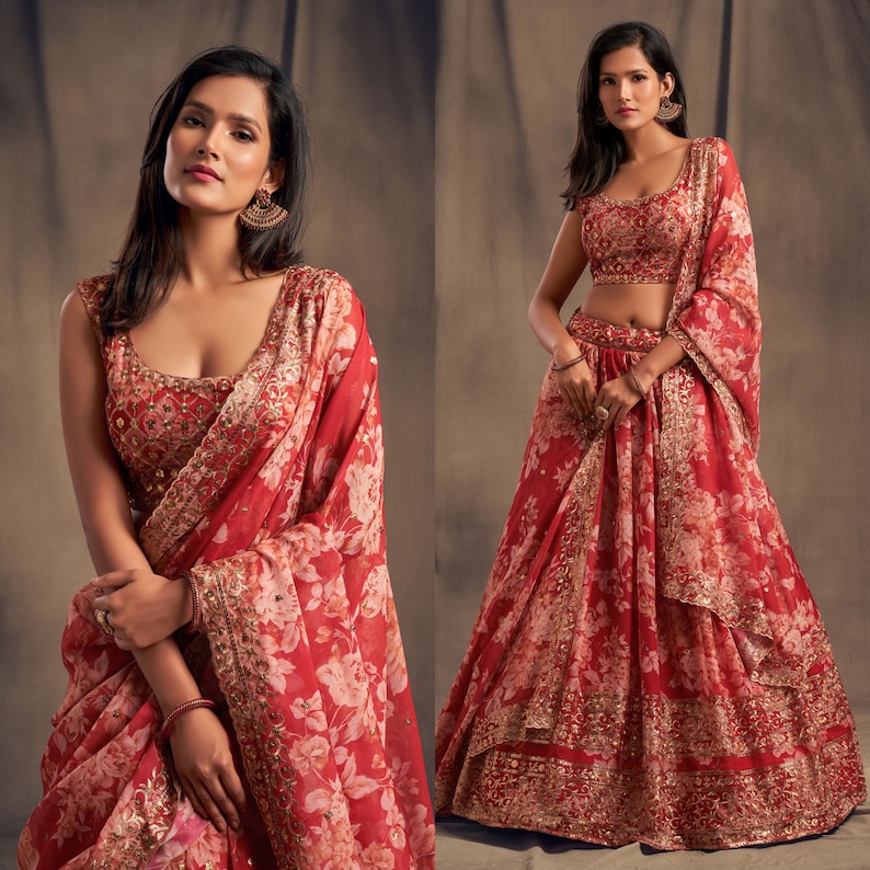 May include: A red floral print lehenga choli ensemble. The outfit features a sleeveless top and a flowing skirt, both adorned with a delicate white floral pattern. The dupatta, or scarf, mirrors the design, with gold embellishments adding a touch of elegance. The outfit is suitable for special occasions.