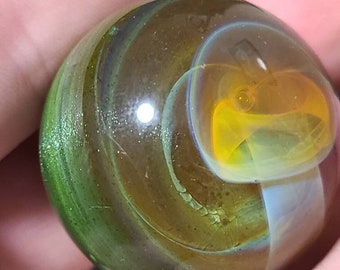 May include: A green, brown and yellow glass marble with swirling patterns. The marble has a shiny, iridescent finish.
