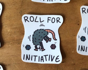 May include: A white sticker with a cartoon possum rolling for initiative. The possum is gray and has a pink nose. The sticker says "Roll for Initiative" in black text.