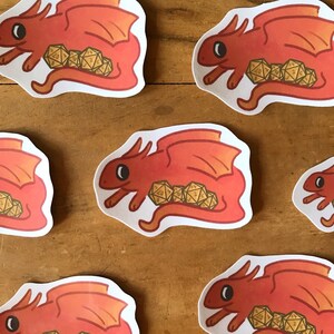 May include: A set of red dragon stickers with gold dice inside. The dragons are curled up with their wings spread out. The stickers are perfect for adding a touch of whimsy to your laptop, water bottle, or planner.