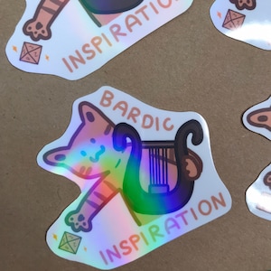 Può includere: Un adesivo olografico con un gatto dei cartoni animati che suona l'arpa con il testo "Ispirazione Bardica".