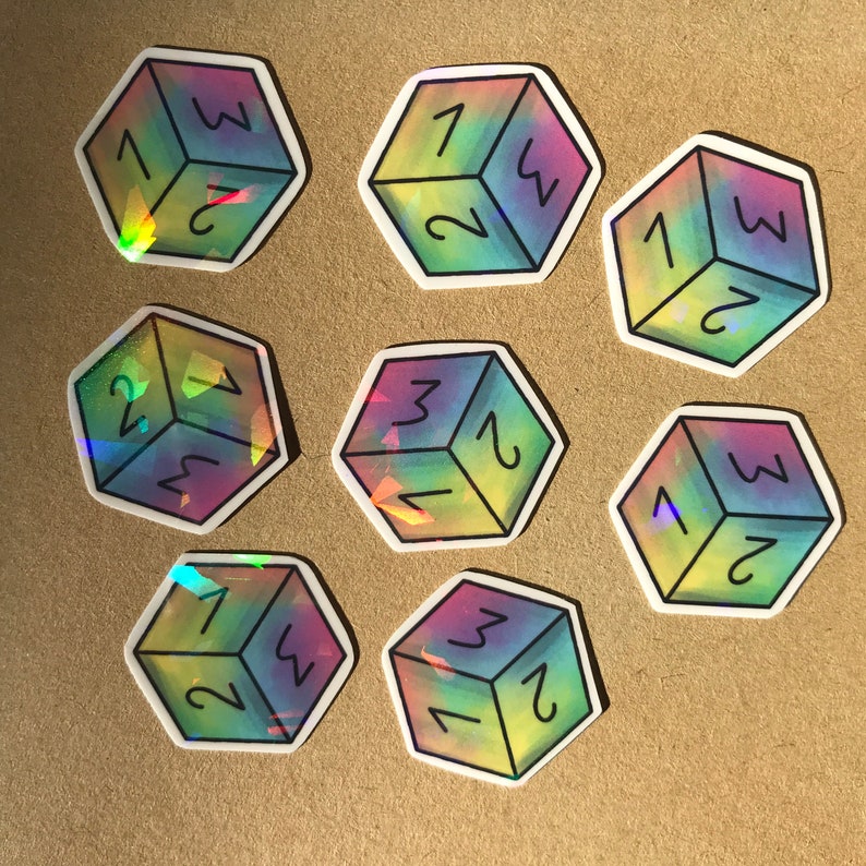 May include: Nine iridescent holographic stickers of a six-sided die with numbers 1 through 6. The stickers are arranged in a circle on a brown surface.