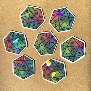 May include: Seven iridescent holographic stickers of a twenty-sided die with black numbers. The stickers are arranged in a circle on a brown surface.