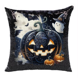Puede incluir: Cojín de Halloween con lentejuelas negras con una calabaza espeluznante con una cara tallada, murciélagos, un fantasma con sombrero de bruja y luna llena. Dos calabazas más pequeñas y una vela encendida completan el diseño festivo.