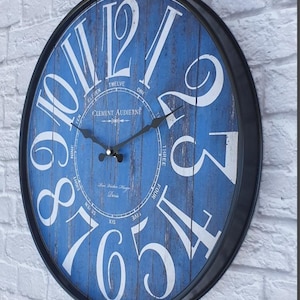 May include: A round wall clock with a distressed blue face and large white numerals. The clock has a black metal frame and black hands. The clock face features the text "Clement Audierne Paris".