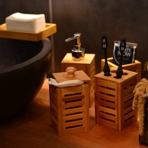 May include: A bathroom vanity with a black sink, a wooden soap dish, a wooden dispenser with a silver pump, and three wooden toothbrush holders with black toothbrushes. The holders are on a wooden countertop.