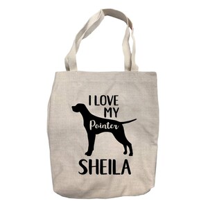 May include: A beige canvas tote bag with black text and a black silhouette of a dog. The text reads "I love my Pointer Sheila".