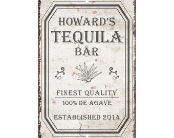 May include: A rustic metal sign with a white background and black text. The sign reads "Howard's Tequila Bar Finest Quality 100% De Agave Established 2014".