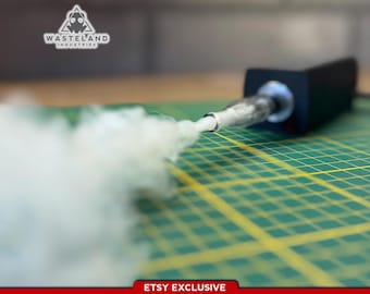 May include: A black handheld device with a metallic nozzle emitting a thick white plume of smoke. The device features the Wasteland Industries logo and text. The item is positioned on a green cutting mat with yellow grid lines and an Etsy Exclusive label.