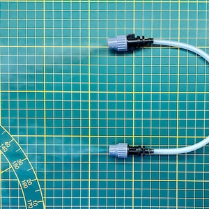 Peut inclure: Un tube en plastique transparent avec deux buses de pulvérisation noires et grises sur un tapis de coupe vert. Le tube est plié en forme de U et les deux buses pulvérisent une fine brume.