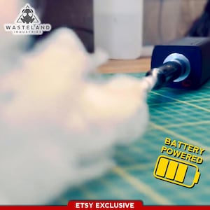 May include: A black, battery-powered electronic device emitting a thick cloud of white vapor. The device features a silver nozzle and a logo in the top left corner reading Wasteland Industries. A yellow battery icon with the text BATTERY POWERED is visible.