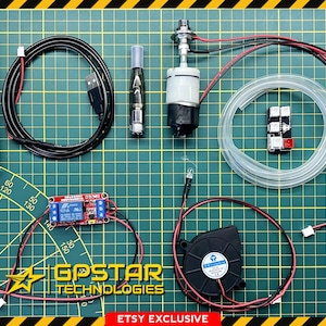 Może przedstawiać: Zestaw elementów elektronicznych, w tym przezroczysta butelka z tekstem, czarny kabel USB, mały wentylator i płytka drukowana. Elementy są ułożone na zielonej powierzchni kratki. Widoczny jest tekst "GPSTAR TECHNOLOGIES".