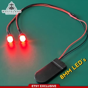 May include: Two bright red 8mm LED lights connected by black and red wires to a black battery pack. The Wasteland Industries logo is visible in the top left corner, and the text 8MM LED's is printed in yellow near the battery pack.