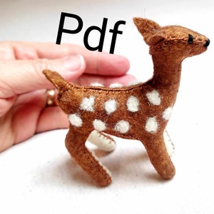 May include: A brown and white spotted felt deer with black eyes. The deer is standing on a white surface.