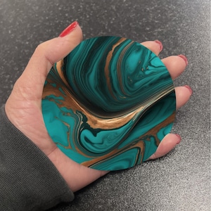 May include: A round coaster featuring a swirling pattern of teal blue and gold. The coaster has a marbled effect.