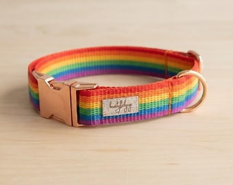 Puede incluir: Un collar para mascotas con rayas de arcoíris hecho de cinta de nailon tejida, con una hebilla de liberación lateral de metal en oro rosa y una anilla en D a juego. Tiene una pequeña etiqueta rectangular plateada con texto cosida.