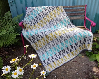 May include: A colorful, handmade crochet blanket draped over a pink bench. The blanket features a geometric pattern in shades of gray, teal, and yellow. The blanket is made of soft yarn and is perfect for adding a touch of warmth and style to any space.
