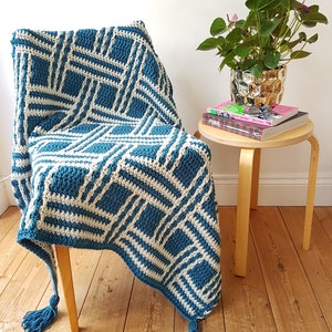 May include: A teal and white crocheted throw blanket with tassels draped over a wooden chair. The blanket has a geometric pattern.