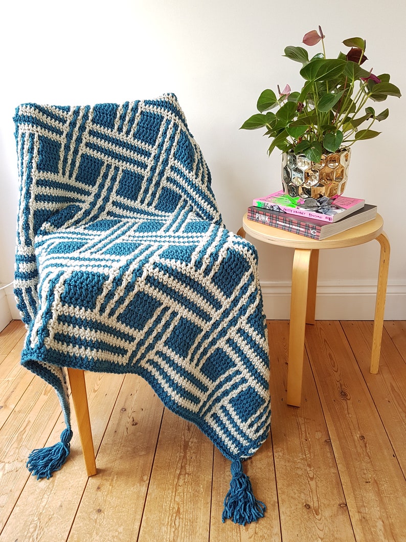 May include: A teal and white crocheted throw blanket with tassels draped over a wooden chair. The blanket has a geometric pattern.