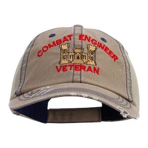 May include: Tan baseball cap with a mesh back and a curved brim. The cap features the embroidered text "COMBAT ENGINEER VETERAN" in red, with a gold and brown castle graphic. The brim and seams have navy blue stitching.