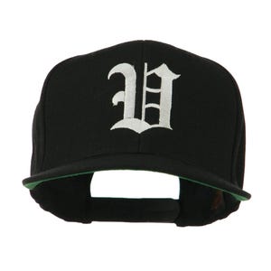 May include: Black baseball cap with a flat brim and a white, stylized letter "H" embroidered on the front. The underside of the brim is green. The cap has an adjustable strap for a comfortable fit.