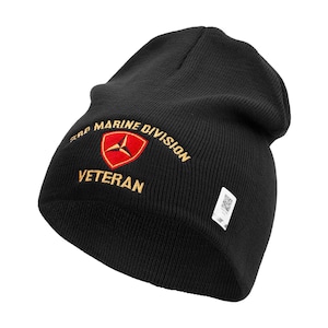 May include: Black knit beanie with the text "3rd Marine Division Veteran" embroidered in gold thread. The design includes a red and gold emblem. A small white tag with a QR code is attached to the side.
