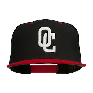 May include: Black baseball cap with a red peak and the letters "OC" in white. The cap has a flat peak and a structured crown. The interior peak is green. The cap is a classic style, suitable for casual wear.