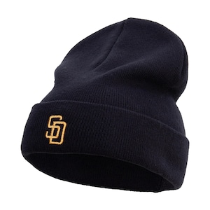May include: Navy blue knit beanie with a folded brim. The beanie features a gold-colored embroidered logo on the front. This winter hat is a stylish accessory for cold weather.