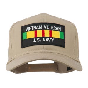 May include: A tan baseball cap with a curved brim. The front features a rectangular patch with the words "VIETNAM VETERAN" above "U.S. NAVY". The patch has green and yellow stripes with red stripes in the center.