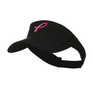 May include: Black visor featuring a pink ribbon emblem. The visor has a curved peak and an adjustable strap. The pink ribbon is a symbol of breast cancer awareness.