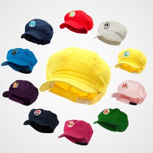May include: A set of 10 colorful hats with different embroidered designs. The hats are all the same style, with a flat top and a brim that curves down around the sides. The designs include a crown, a star, a mushroom, a letter L, a letter M, a letter N, a bomb, a ghost, and a question mark.