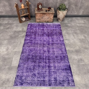 May include: A rectangular area rug featuring a deep purple color with a distressed, faded texture. The rug has a uniform, solid-toned appearance with subtle variations in shade across its surface, creating a worn, weathered look.