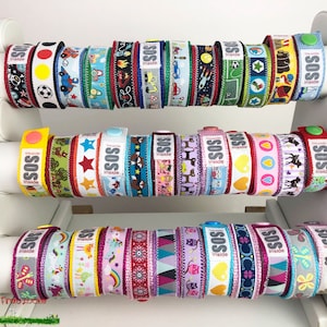 May include: A display of colorful fabric wristbands with the word "SOS" and the text "Inside" printed on them. The wristbands feature various designs, including animals, stars, hearts, and geometric patterns.