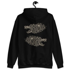 Puede incluir: Una sudadera con capucha negra que presenta un estampado gr&aacute;fico en la parte posterior. El dise&ntilde;o consta de dos cabezas de lobo de color beige detalladas en perfil, mirando en direcciones opuestas con las fauces abiertas.