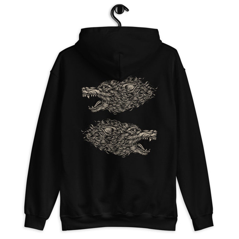 Puede incluir: Una sudadera con capucha negra que presenta un estampado gr&aacute;fico en la parte posterior. El dise&ntilde;o consta de dos cabezas de lobo de color beige detalladas en perfil, mirando en direcciones opuestas con las fauces abiertas.
