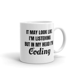 May include: White ceramic mug with a black handle. The mug features the text "IT MAY LOOK LIKE I'M LISTENING BUT IN MY HEAD I'M Coding" in a black, bold font. The mug is designed for coffee, tea, or other beverages.