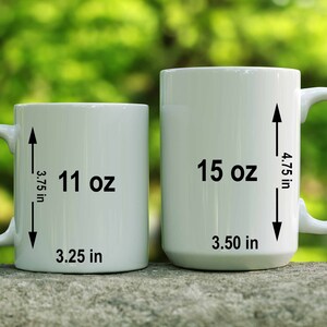 May include: Two white ceramic mugs with black markings. The smaller mug is 11 oz and 3.25 inches wide. The larger mug is 15 oz and 3.5 inches wide.