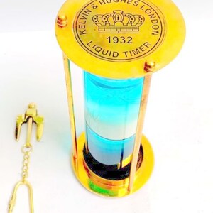 May include: A brass hourglass with a blue and white liquid inside. The top of the hourglass has an inscription that reads "Kelvin & Hughes London 1932 Liquid Timer". A small brass anchor keychain is included.